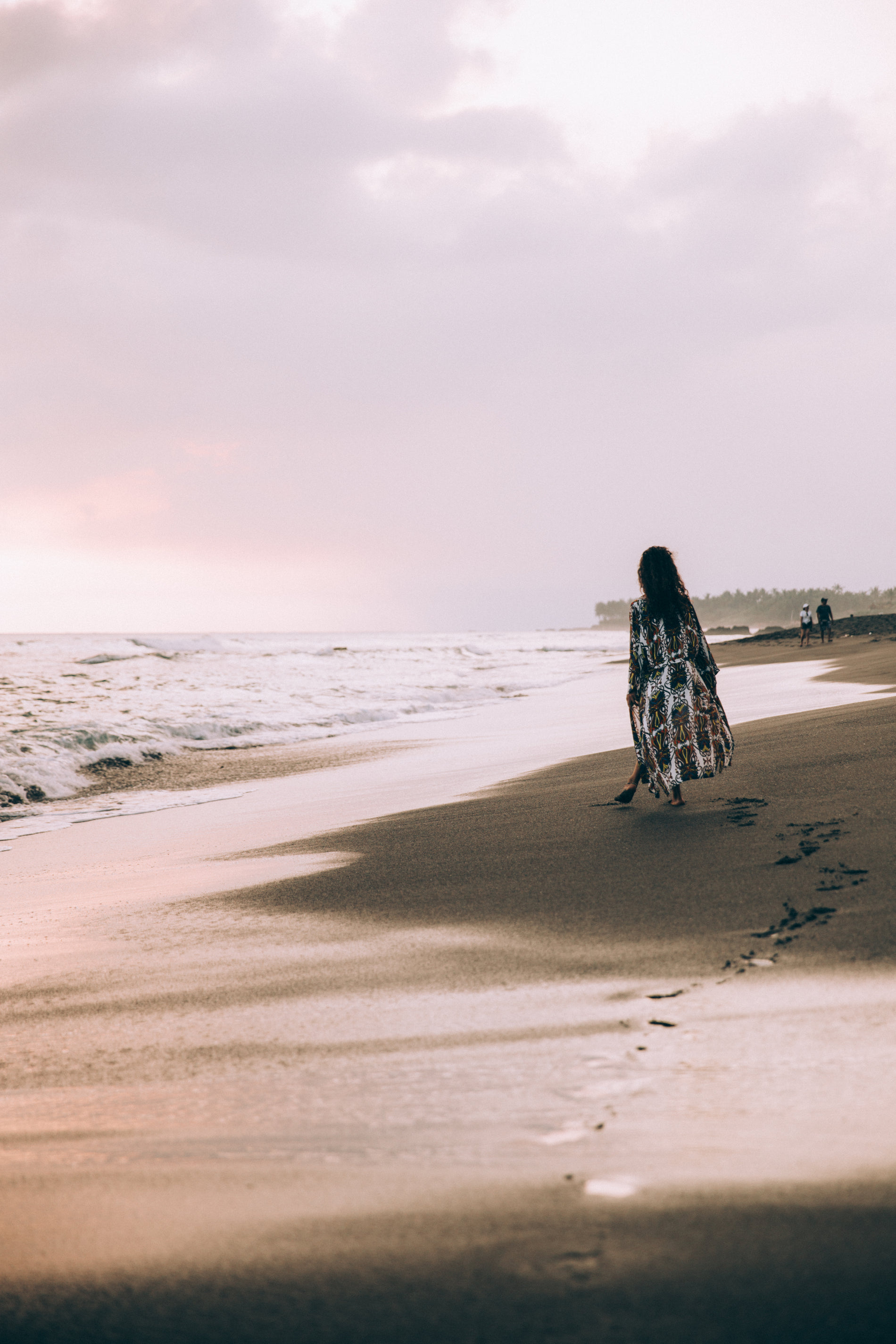 Woman in a printed dress walking along the shoreline at sunset