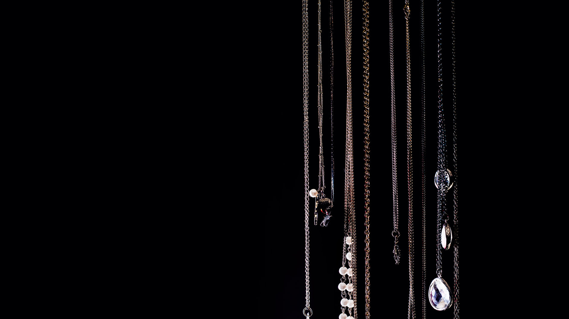 Rows of fine gold and silver chains hanging against a dark background